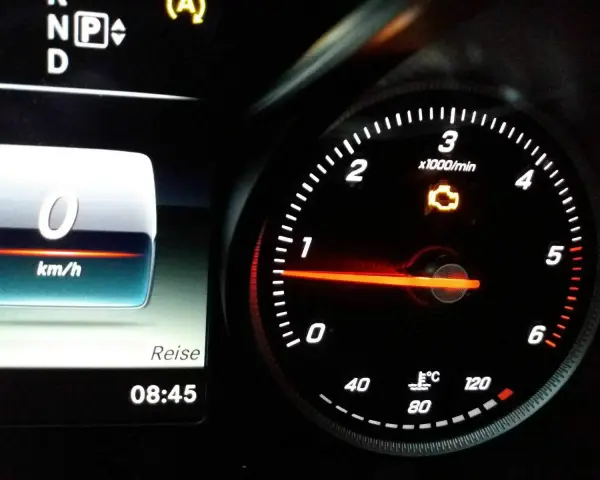 Mercedes-Armaturenbrett mit leuchtender Motorkontrollleuchte. Tachometer zeigt 0 km/h, daneben die Uhrzeit 08:45.