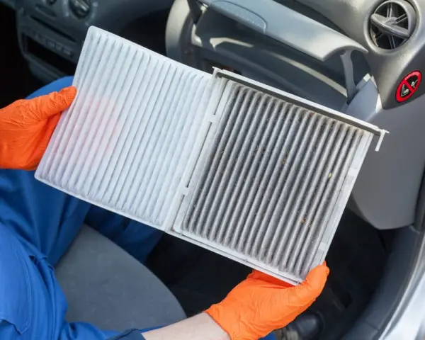 Person mit orangefarbenen Handschuhen hält einen neuen und einen schmutzigen Innenraumfilter. Zeit, den Innenraumfilter zu wechseln für saubere Luft im Auto.
