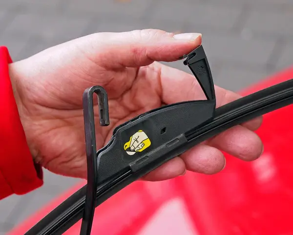 Hand wechselt Scheibenwischer an einem VW. Der Haken des Wischerarms wird in die Halterung eingeführt.