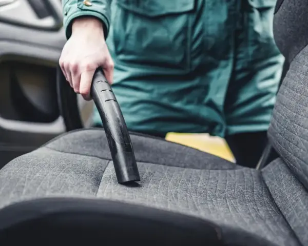 Person reinigt den auto innenraum mit einem Staubsauger.