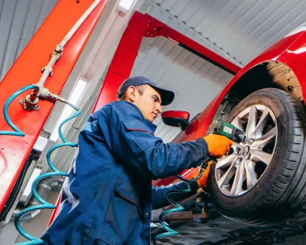 Mechaniker wechselt Reifen an rotem Auto. Informieren Sie sich, was kostet reifenwechsel, um Ihr Fahrzeug sicher zu halten.