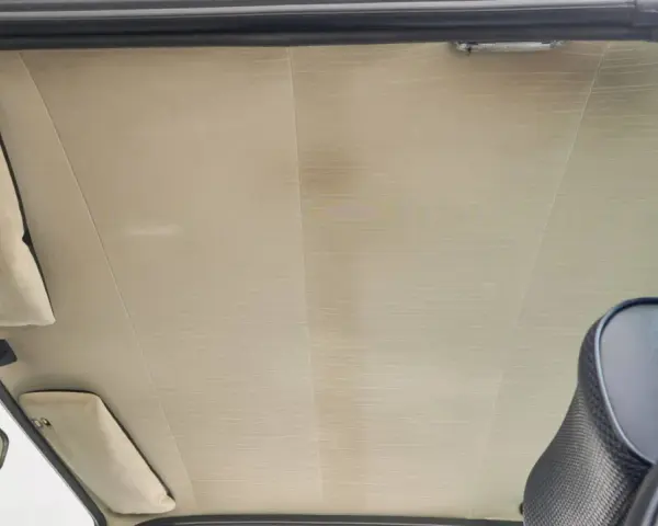 Der Dachhimmel kleben ist eine Kunst. Hier sieht man den hellen, gemusterten Dachhimmel eines Autos, mit Sonnenblenden und Rückspiegel.