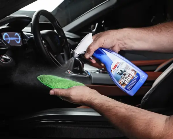 Mann sprüht Reinigungsmittel auf ein Mikrofasertuch, um Kunststoff im Auto zu reinigen.