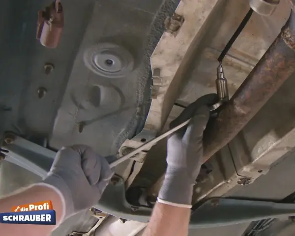Ein Mechaniker löst die Lambdasonde am Auspuffrohr. Sie sitzt im vorderen Teil des Rohrs, nahe am Motor.