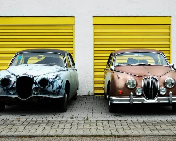 Zwei Oldtimer vor gelben Garagentoren. Einer ist rostig, der andere glänzt. Die **Oldtimer Lackieren Kosten** variieren stark.
