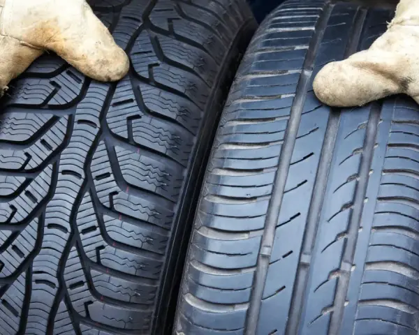 Zwei Reifen werden von Händen in Arbeitshandschuhen gehalten. Links ein Winterreifen, rechts ein Sommerreifen. Darf man mit Winterreifen im Sommer fahren?