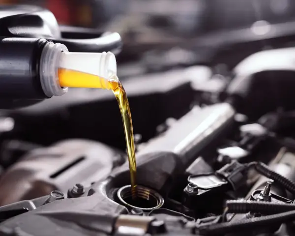Frisches Öl fließt aus einer Flasche in einen Motor. Die API-Klassifikation des Öls ist entscheidend für die Leistung.