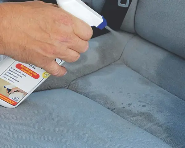 Hand sprüht Flecken aus Autositz mit Reiniger.