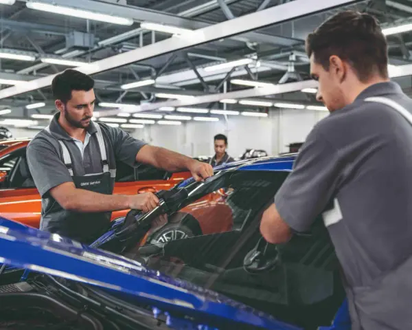 Zwei Mechaniker führen einen BMW Fahrzeugcheck durch. Einer entfernt die Windschutzscheibe, der andere sichert sie.