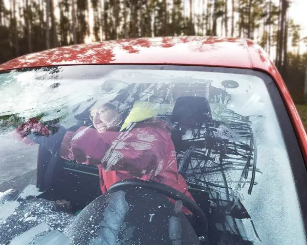 Frau versucht, die vereiste Autoscheibe innen freizukratzen. Tipps zur Vorbeugung von vereister Autoscheibe innen.