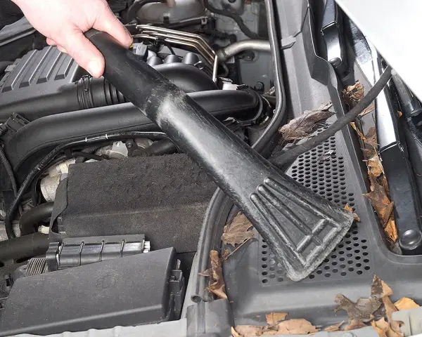 Hand saugt Laub und Schmutz aus dem Motorraum, um Feuchtigkeit im Auto vorzubeugen.