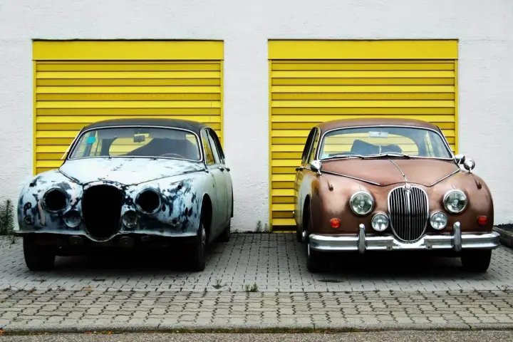 Zwei Oldtimer vor gelben Garagentoren. Einer ist rostig, der andere glänzt. Die **Oldtimer Lackieren Kosten** variieren stark.