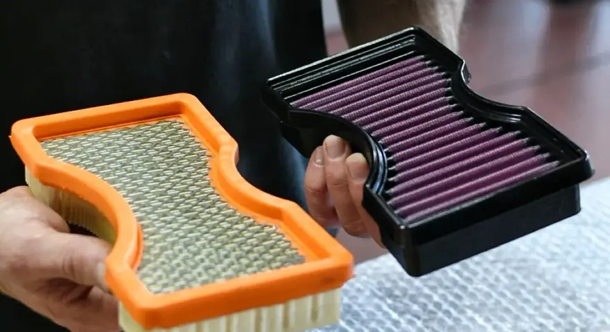Hände halten zwei Luftfilter: einen orangen Standardfilter und einen schwarzen Sportluftfilter. Was bringt ein Sportluftfilter? Mehr Leistung!