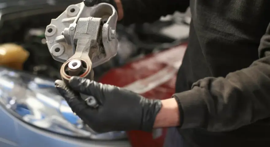 Mechaniker hält ein defektes Motorlager in der Hand, das ausgetauscht werden muss.