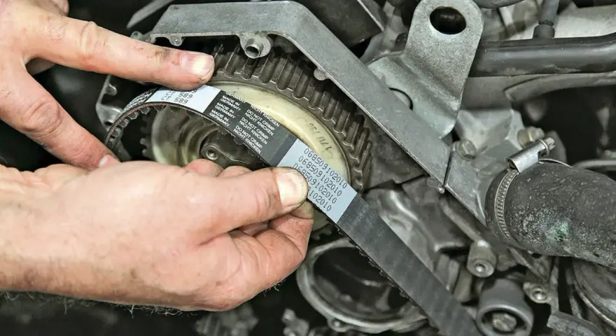 Hände montieren einen neuen Zahnriemen an einem Motor. So gelingt der Zahnriemenwechsel selbst.
