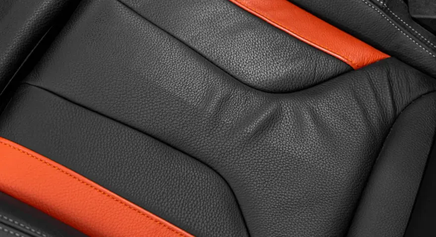 Detailaufnahme eines schwarzen Ledersitzes mit orangefarbenen Akzenten. Perfekt für die Leder reinigen Pflege.