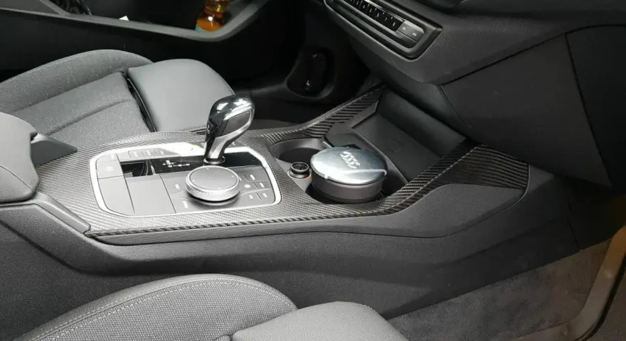 Detailaufnahme des Innenraums eines Autos mit Carbon-Akzenten. Ein Aschenbecher mit Audi-Logo steht im Getränkehalter. So reinigt man klavierlack auto.