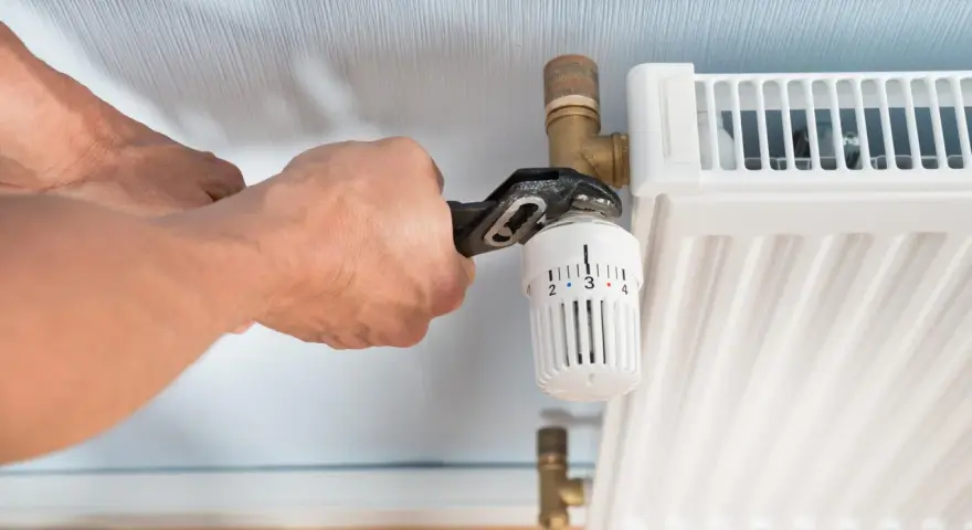 Hände wechseln einen Heizkörperthermostat mit einer Rohrzange.