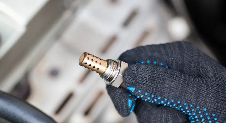 Defekte Lambdasonde als Ursache für die Motorkontrollleuchte. Ein Mechaniker hält das Bauteil in der Hand.