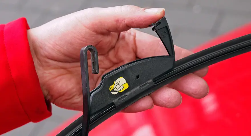 Hand wechselt Scheibenwischer an einem VW. Der Haken des Wischerarms wird in die Halterung eingeführt.