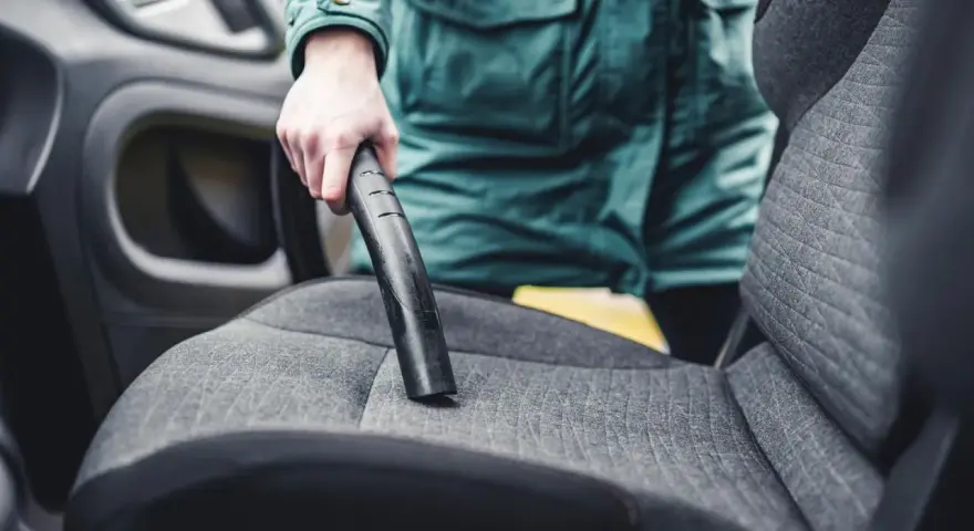 Person reinigt den auto innenraum mit einem Staubsauger.