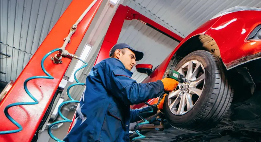 Mechaniker wechselt Reifen an rotem Auto. Informieren Sie sich, was kostet reifenwechsel, um Ihr Fahrzeug sicher zu halten.