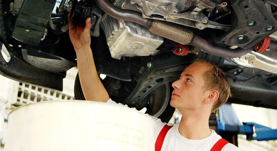 Ein junger Mechaniker bei einer Arbeitsstunde in der Kfz Werkstatt wechselt den Ölfilter unter einem Auto.