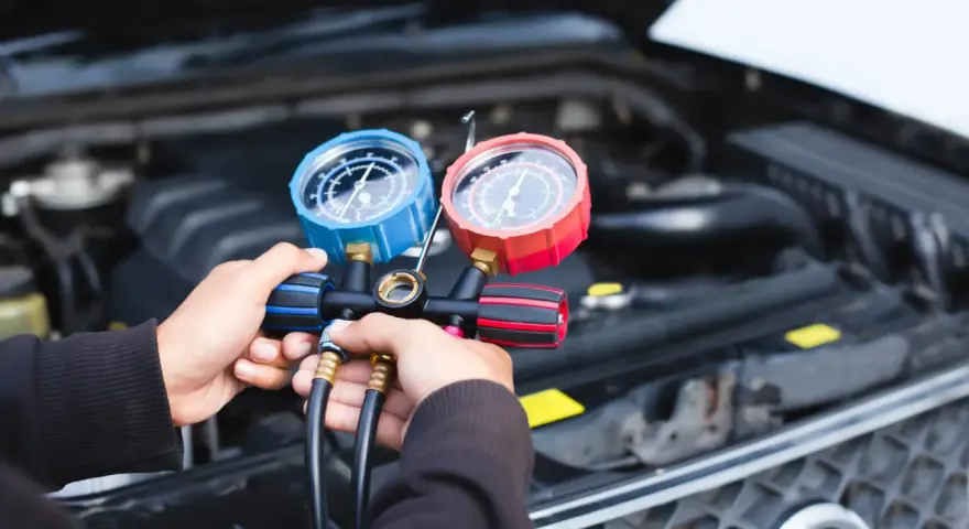 Hände halten ein Klimaanlagen-Manometer-Set, um den Druck zu prüfen. Dies ist ein Schritt zur Ermittlung der klimaanlage reparieren kosten.