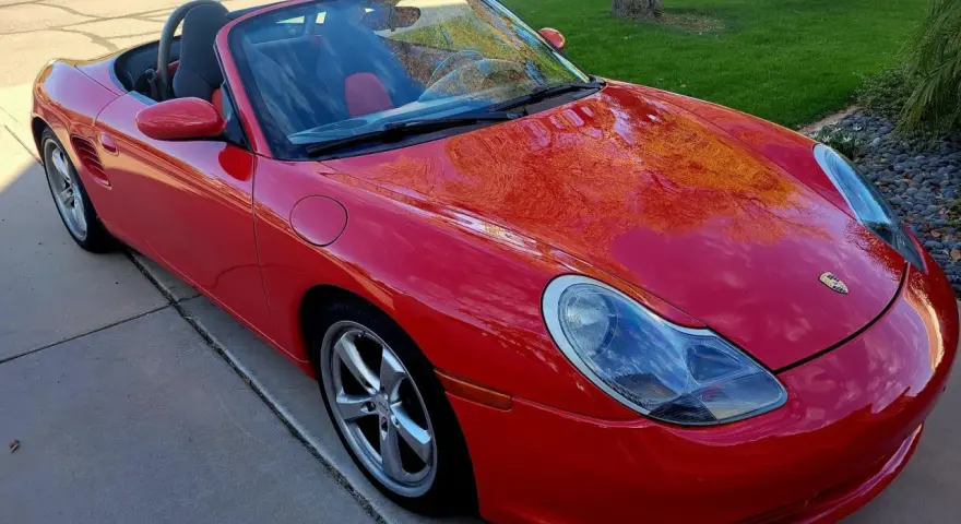 Roter Porsche Boxster Cabriolet. Die glänzende Karosserie spiegelt den Himmel wider. Ein Blick auf die potenziellen Porsche Service Kosten.