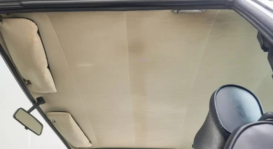Der Dachhimmel kleben ist eine Kunst. Hier sieht man den hellen, gemusterten Dachhimmel eines Autos, mit Sonnenblenden und Rückspiegel.