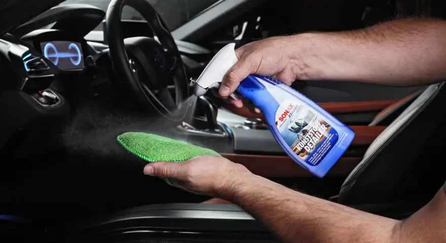 Mann sprüht Reinigungsmittel auf ein Mikrofasertuch, um Kunststoff im Auto zu reinigen.