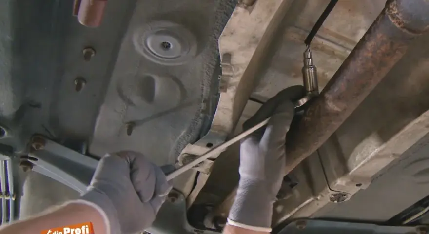 Ein Mechaniker löst die Lambdasonde am Auspuffrohr. Sie sitzt im vorderen Teil des Rohrs, nahe am Motor.