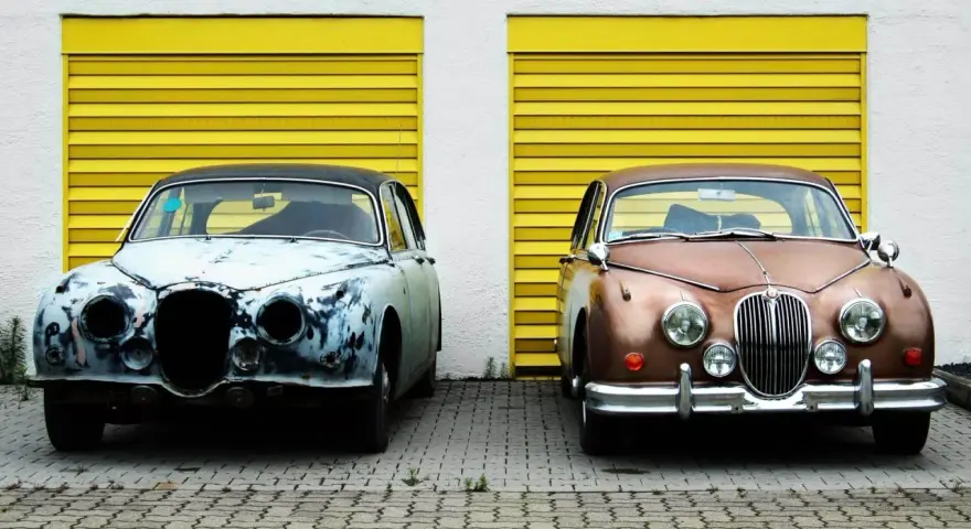 Zwei Oldtimer vor gelben Garagentoren. Einer ist rostig, der andere glänzt. Die **Oldtimer Lackieren Kosten** variieren stark.