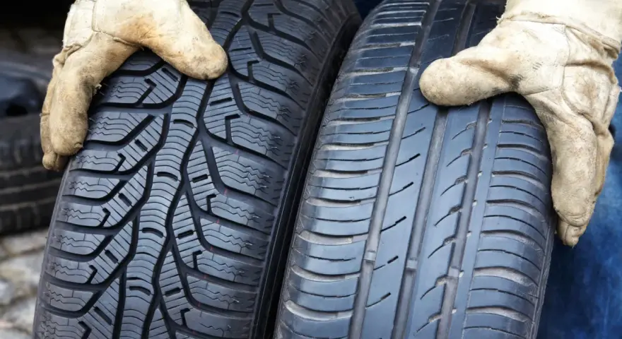 Zwei Reifen werden von Händen in Arbeitshandschuhen gehalten. Links ein Winterreifen, rechts ein Sommerreifen. Darf man mit Winterreifen im Sommer fahren?