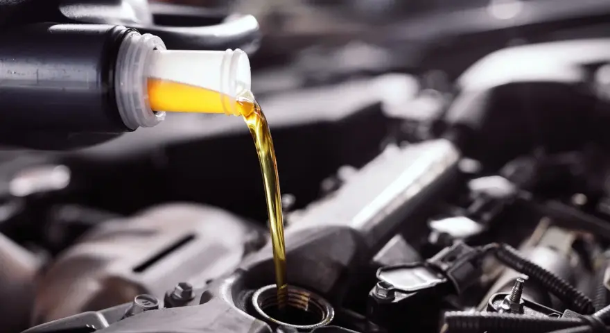 Frisches Öl fließt aus einer Flasche in einen Motor. Die API-Klassifikation des Öls ist entscheidend für die Leistung.