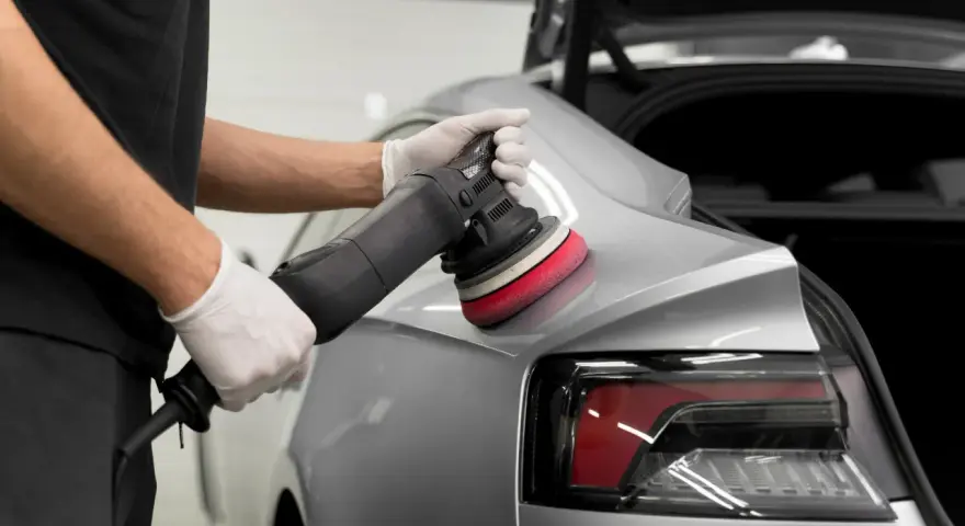 Detailarbeit beim **Lack polieren Auto**. Ein Mann mit Handschuhen nutzt eine Poliermaschine, um den glänzenden Lack auf Hochglanz zu bringen.