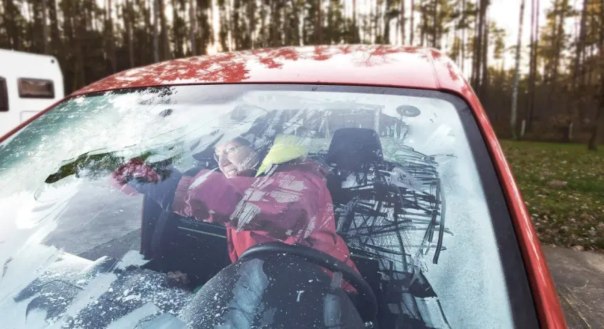 Frau versucht, die vereiste Autoscheibe innen freizukratzen. Tipps zur Vorbeugung von vereister Autoscheibe innen.