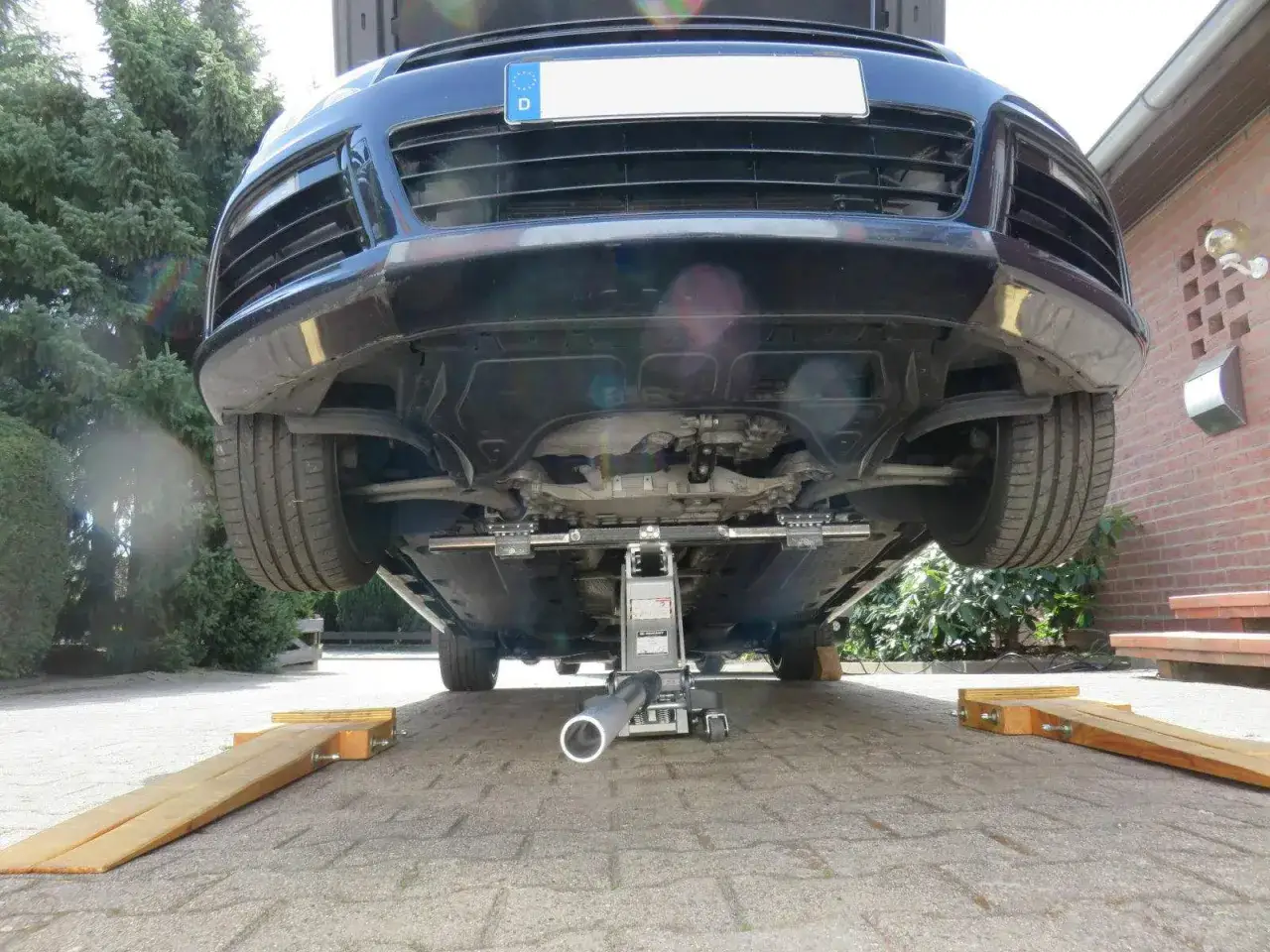 Auto wird mit Wagenheber aufgebockt, um darunter arbeiten zu können. Holzkeile sichern das Fahrzeug.