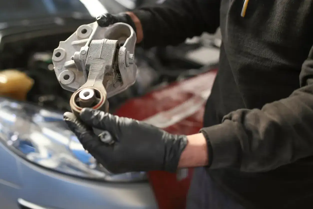 Mechaniker hält ein ausgebautes Teil, das auf einen defekten Motorlager hindeutet.