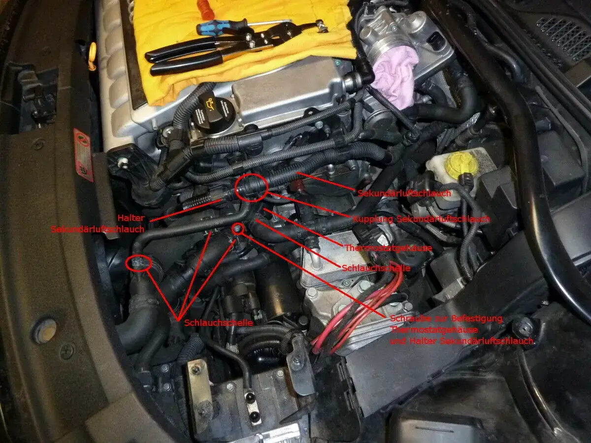 Motorraum mit Werkzeug. Anleitung zum Thermostat wechseln Auto, mit markierten Schläuchen und Gehäusen.