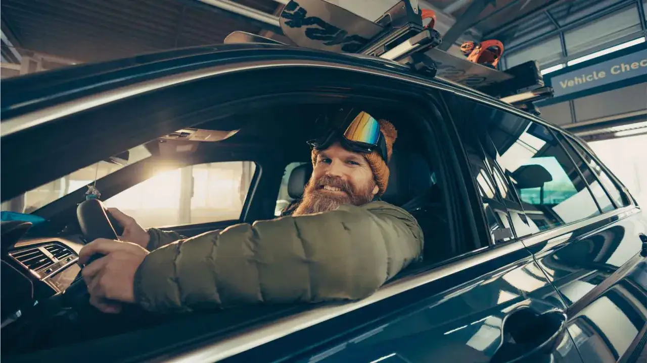 Skifahrer mit Skiern auf dem Dach macht einen Kfz Wintercheck, bereit für die Piste.