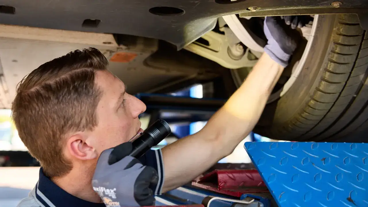 Mechaniker pr&uuml;ft mit Taschenlampe das Fahrwerk. So werden die hu auto kosten niedrig gehalten.