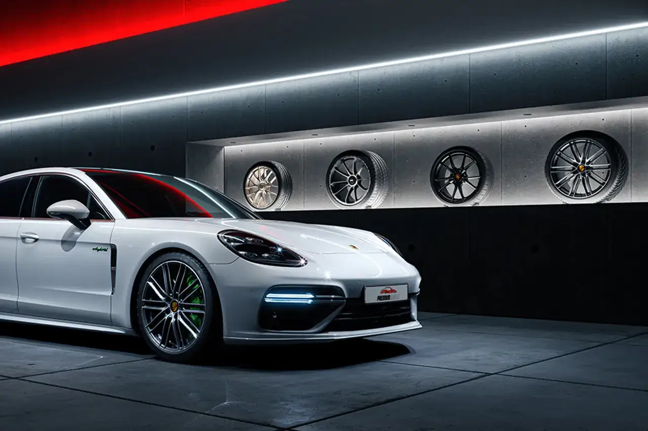 Wei&szlig;er Porsche mit teuren Felgen und vier ausgestellten R&auml;dern an der Wand.