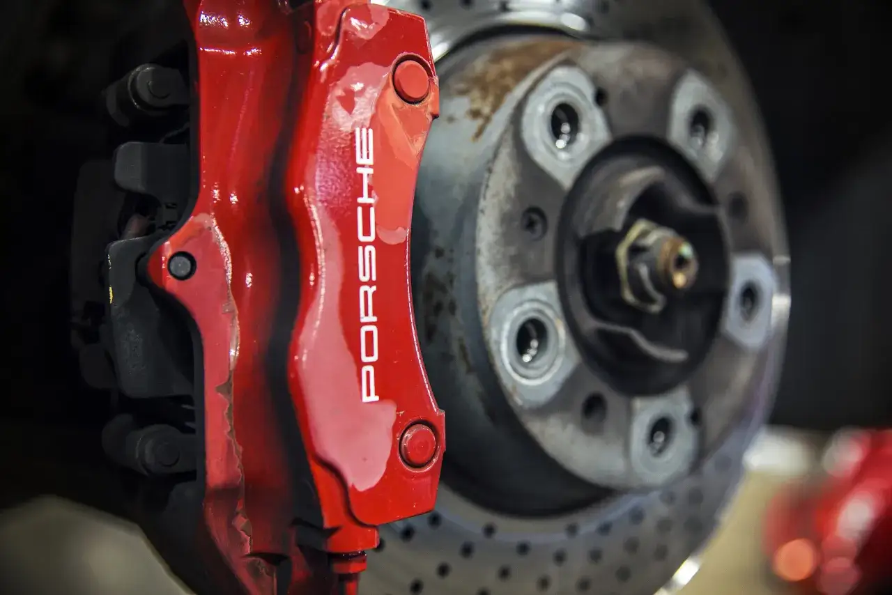 Roter Porsche-Bremssattel über gelochten Bremsscheiben. Gelochte Bremsscheiben Vorteil: bessere Kühlung und Bremsleistung.