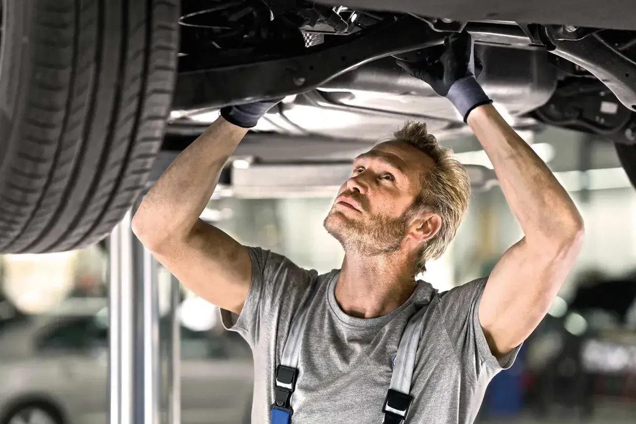 Mechaniker mit Handschuhen prüft unter dem Auto, eine kleine Inspektion Checkliste im Kopf.