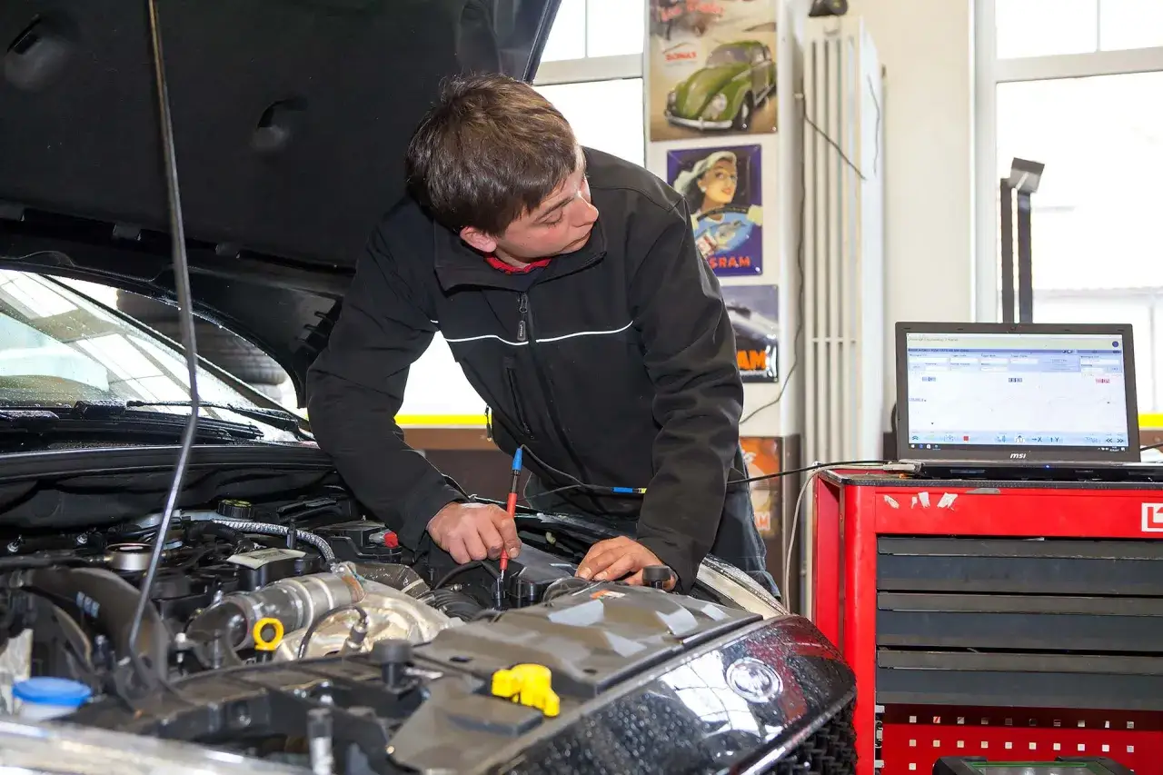 Mechaniker pr&uuml;ft Motor, da das Auto nicht mehr richtig beschleunigt. Diagnoseger&auml;t und Laptop sind angeschlossen.