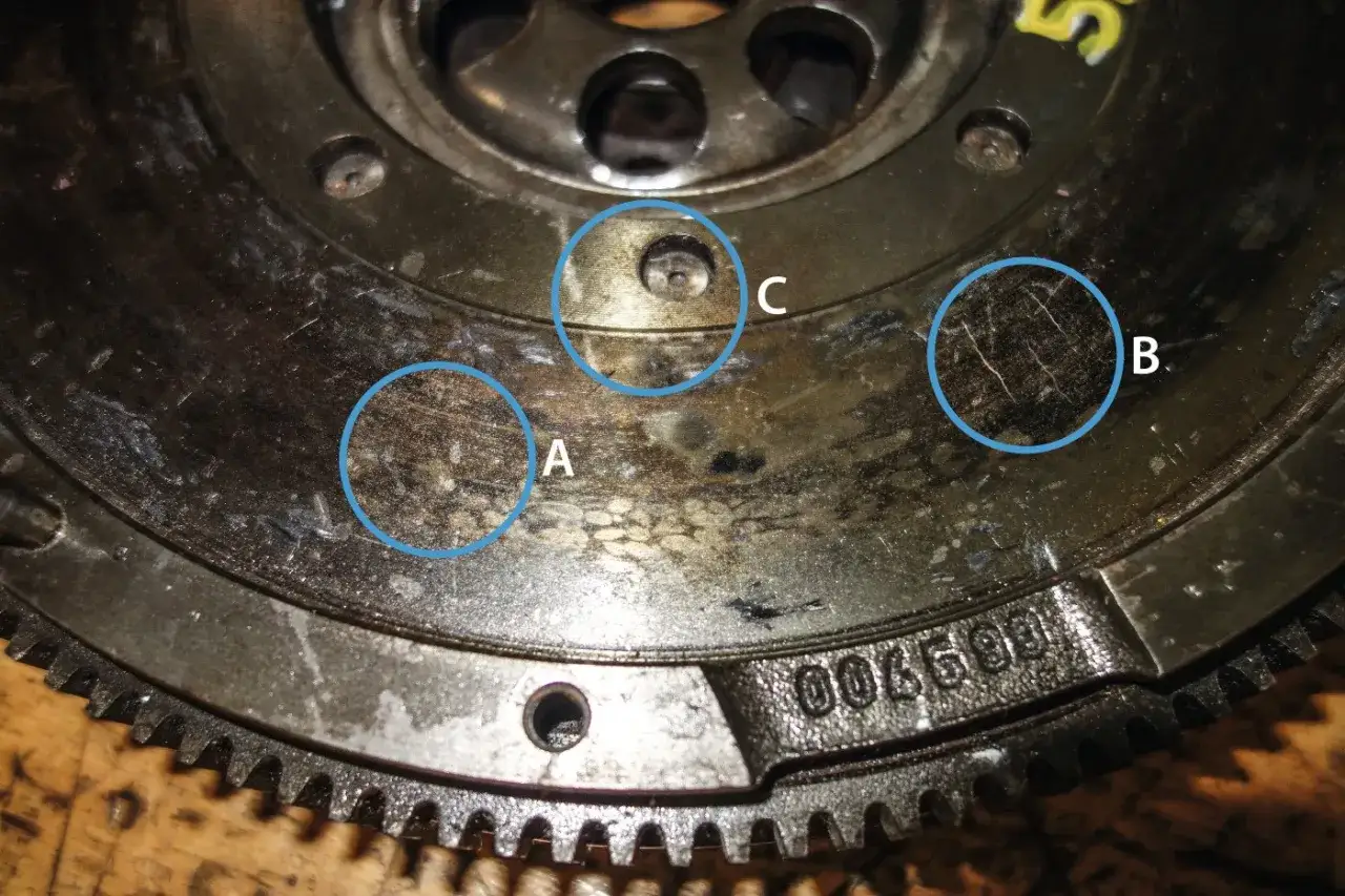 Nahaufnahme einer verschlissenen Schwungscheibe Auto mit markierten Bereichen (A, B, C), die Abnutzungsspuren und Kratzer zeigen.