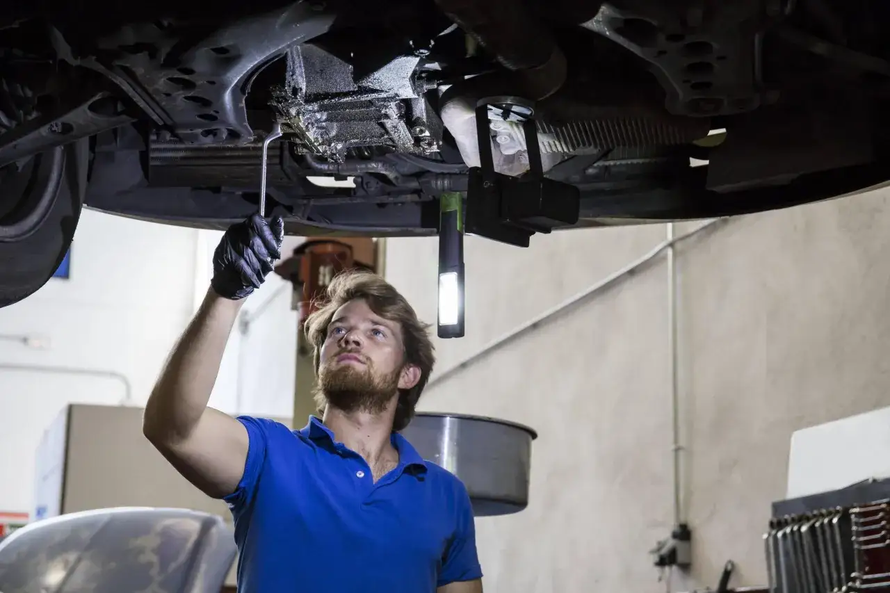 Mechaniker prüft unter dem Auto, fragt sich, wie lange Garantie auf Reparatur und Ersatzteile Auto ist.