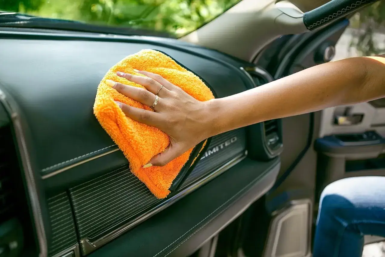 Eine Hand mit orangefarbenem Mikrofasertuch reinigt das Armaturenbrett. So wird der auto innenraum reinigen zum Kinderspiel.