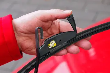 Hand wechselt Scheibenwischer an einem VW. Der Haken des Wischerarms wird in die Halterung eingeführt.